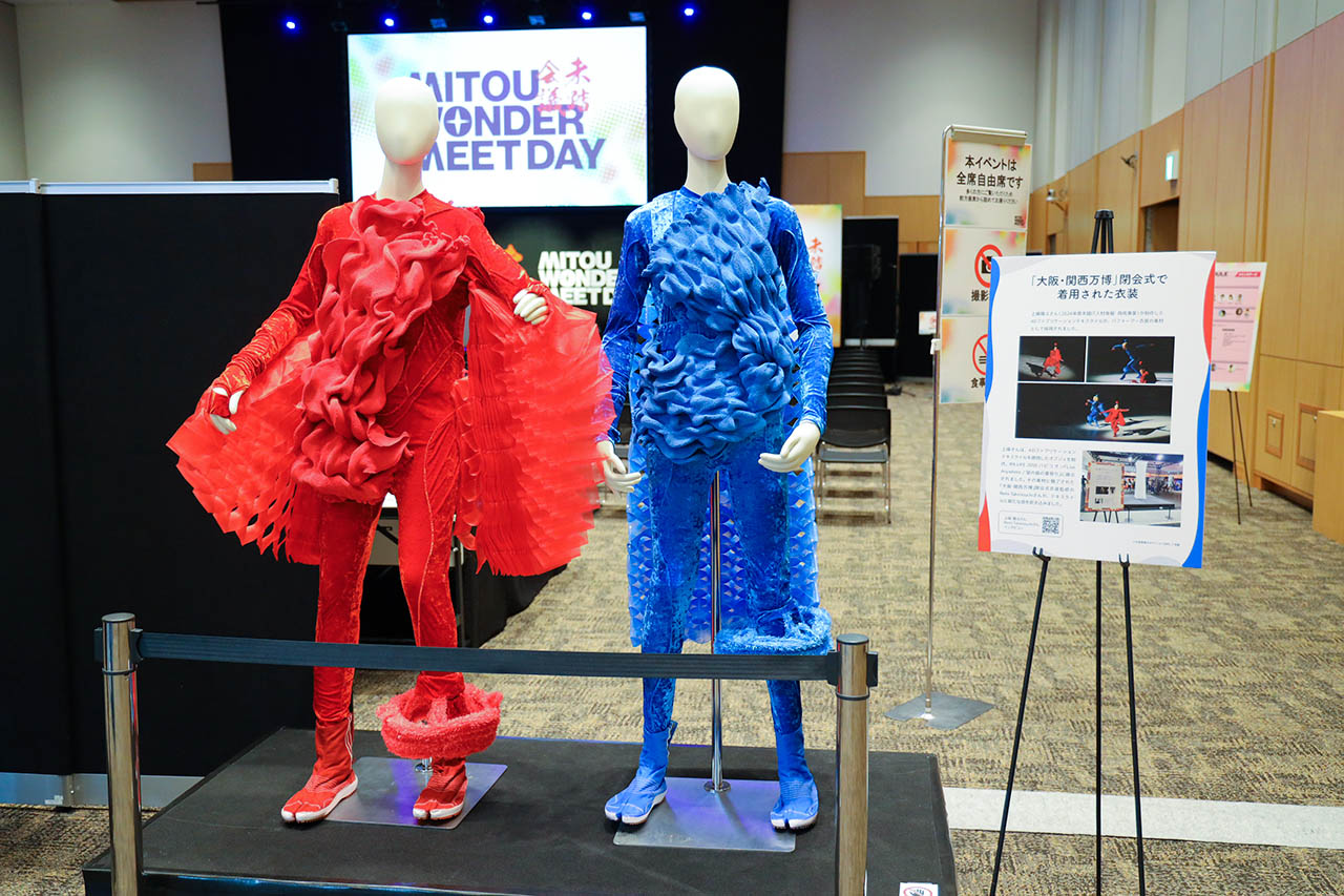万博閉会式で使用された4Dファブリケーションテキスタイルの衣装（赤・青）を着せたマネキン2体の展示と解説パネル